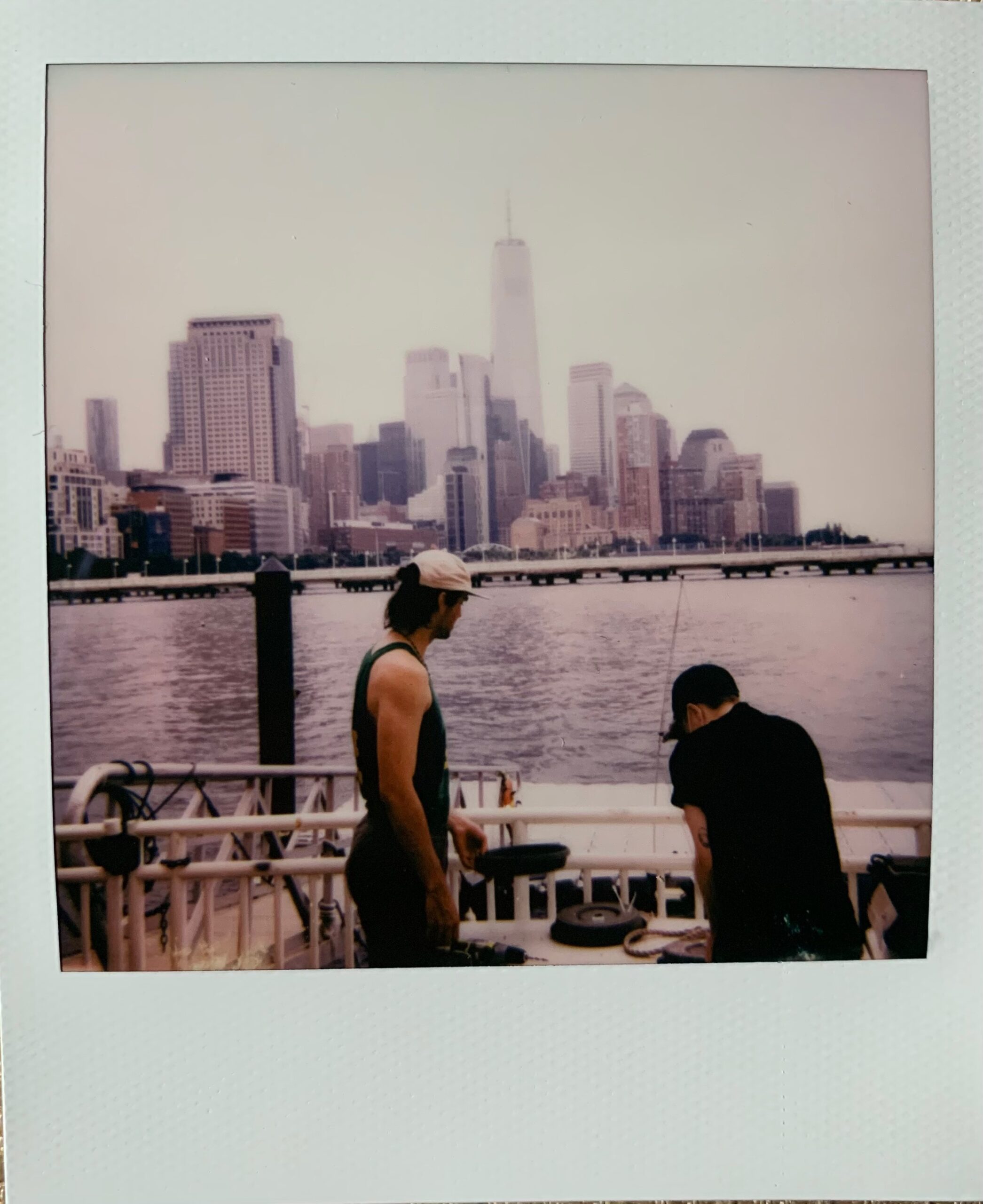 Slater and Jesse work on the mops with their backs turned to the camera. The Hudson River and lower Manhattan are seen in the distance.