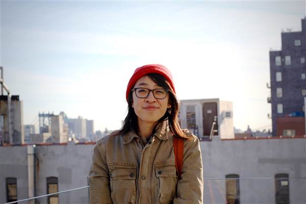 girl with glasses and red hat standing in front of building skyline