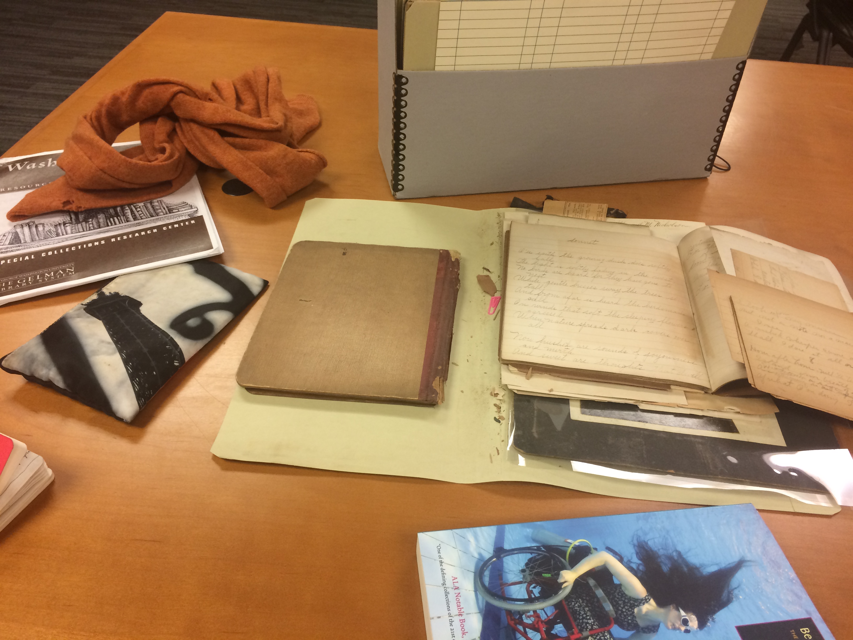 table covered with various items (papers, folder, and scarf)