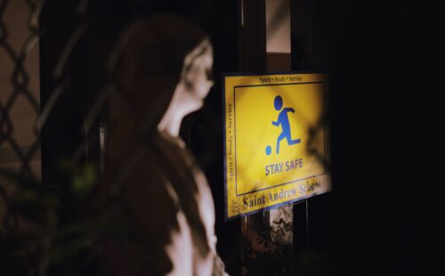 A statue of Mother Mary facing a sign of a child at play, captioned "Stay Safe"