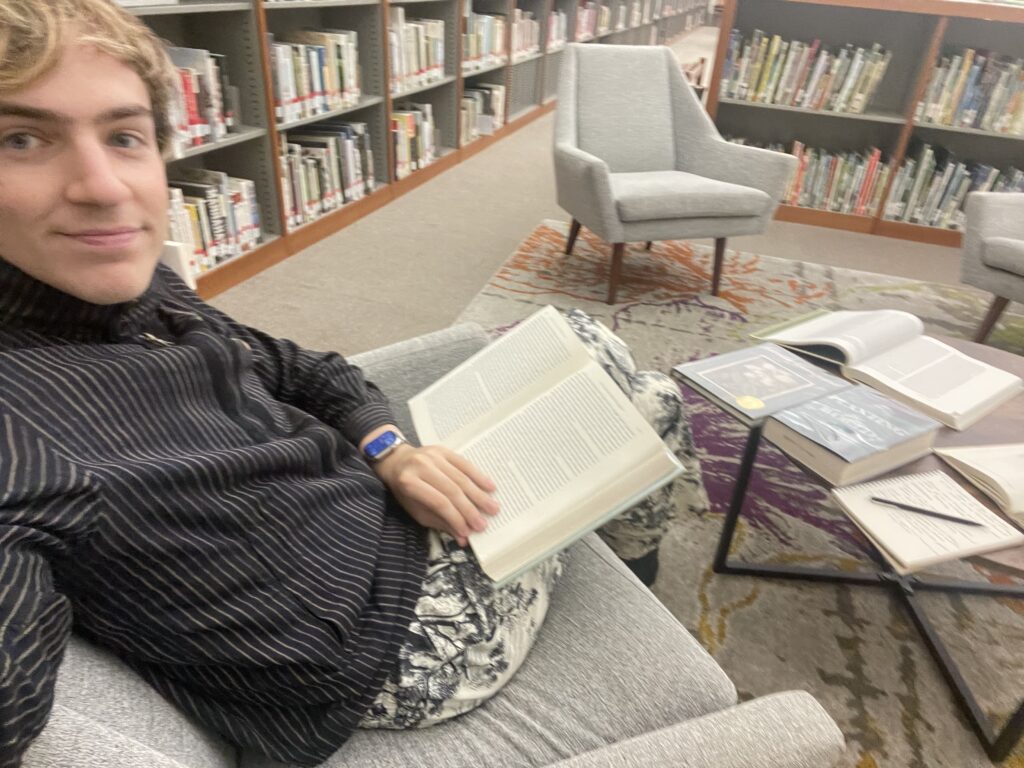Author sitting in a chair in a library reading a book